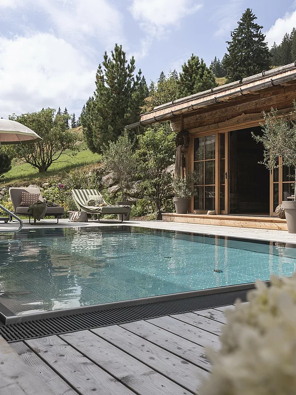 Outdoor-Pool des Chalet Die Schmiedalm in Saalbach Hinterglemm im Sommer mit Chalet und Bergpanorama.